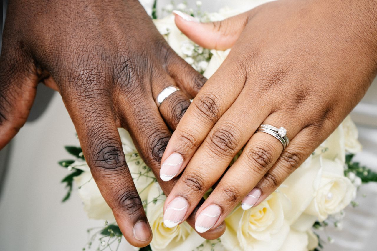 gallery-03 Intimate close-up of wedding rings on a couple's hands over a white rose bouquet.