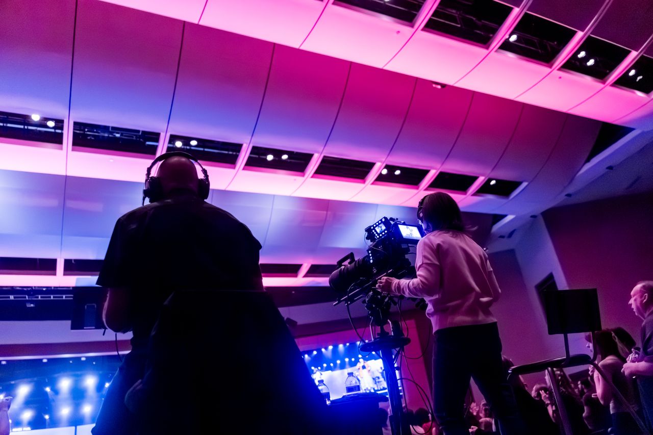portfolio-06 Professional camera crew filming a live event indoors, capturing vibrant stage lighting.